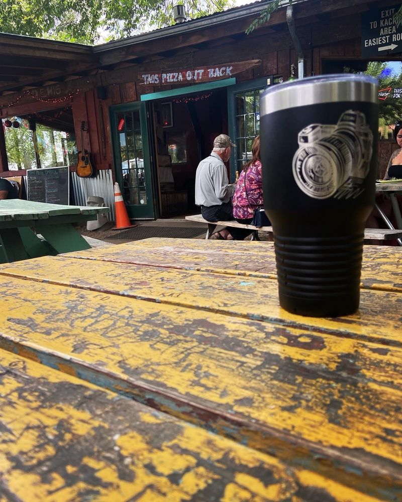 Hand-painted Taos Pizza Out Back sign above the patio picnic tables