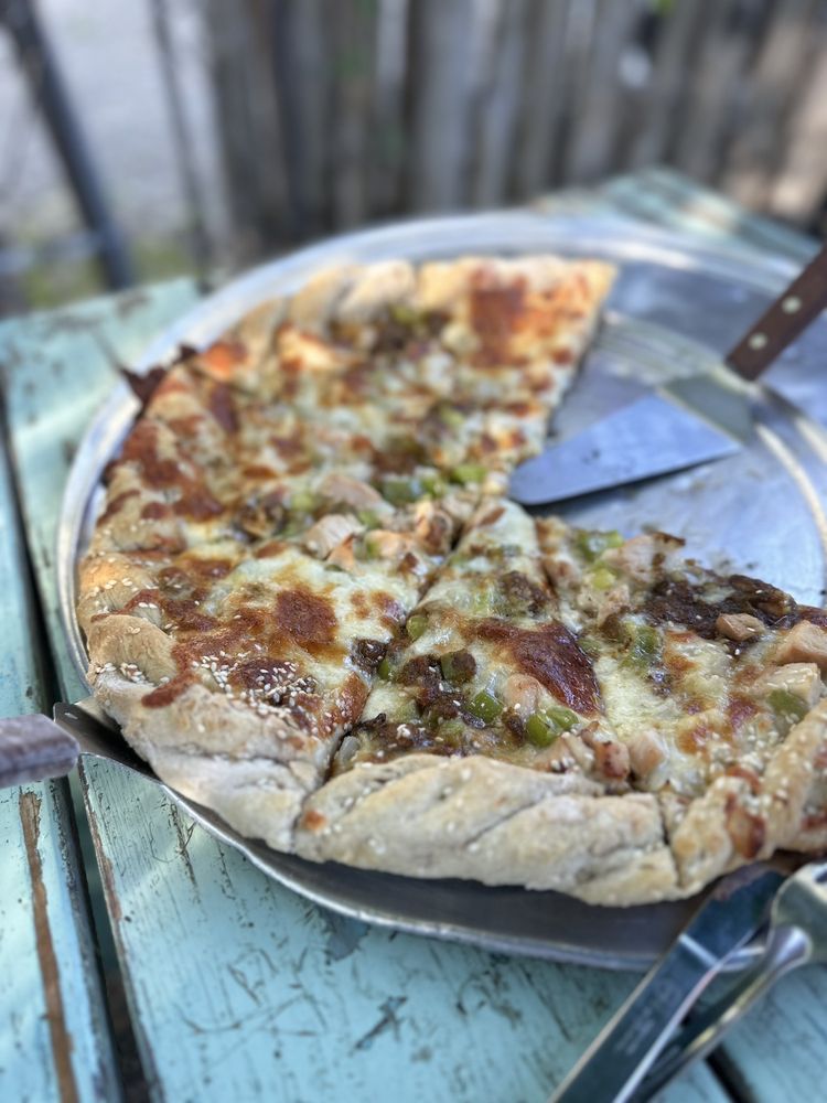 Chicken and green chile pizza on a metal pan at an outdoor table